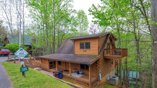 Une cabane en rondins dotée d’un porche, d’une petite terrasse et d’un escalier menant à un balcon.