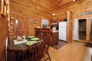 A wooden cabin interior with a dining table, chairs, a kitchen area, and a door leading outside. - 2 king bedrooms, hot tub, great location! (Sevierville)