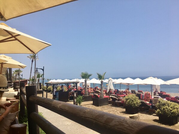 Ein Café am Strand mit Außenbereich und Sonnenschirmen, mit Blick aufs Meer.