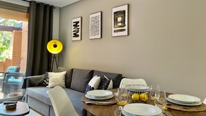 Un salon moderne avec un canapé, une table à manger pour deux personnes et une grande fenêtre agrémentée de rideaux.