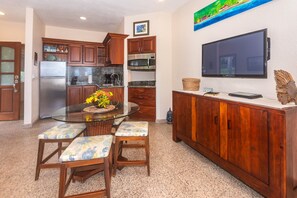 Una cocina compacta con zona de comedor, un televisor de pantalla plana en la pared y un mueble pequeño con una cesta tejida encima.