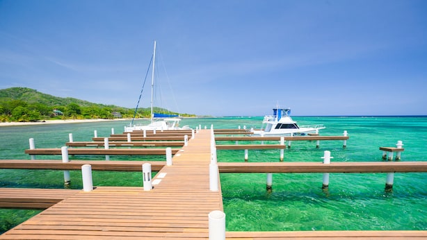 Eine hölzerne Pier, die zu einem Hafen mit vertäuten Booten führt.