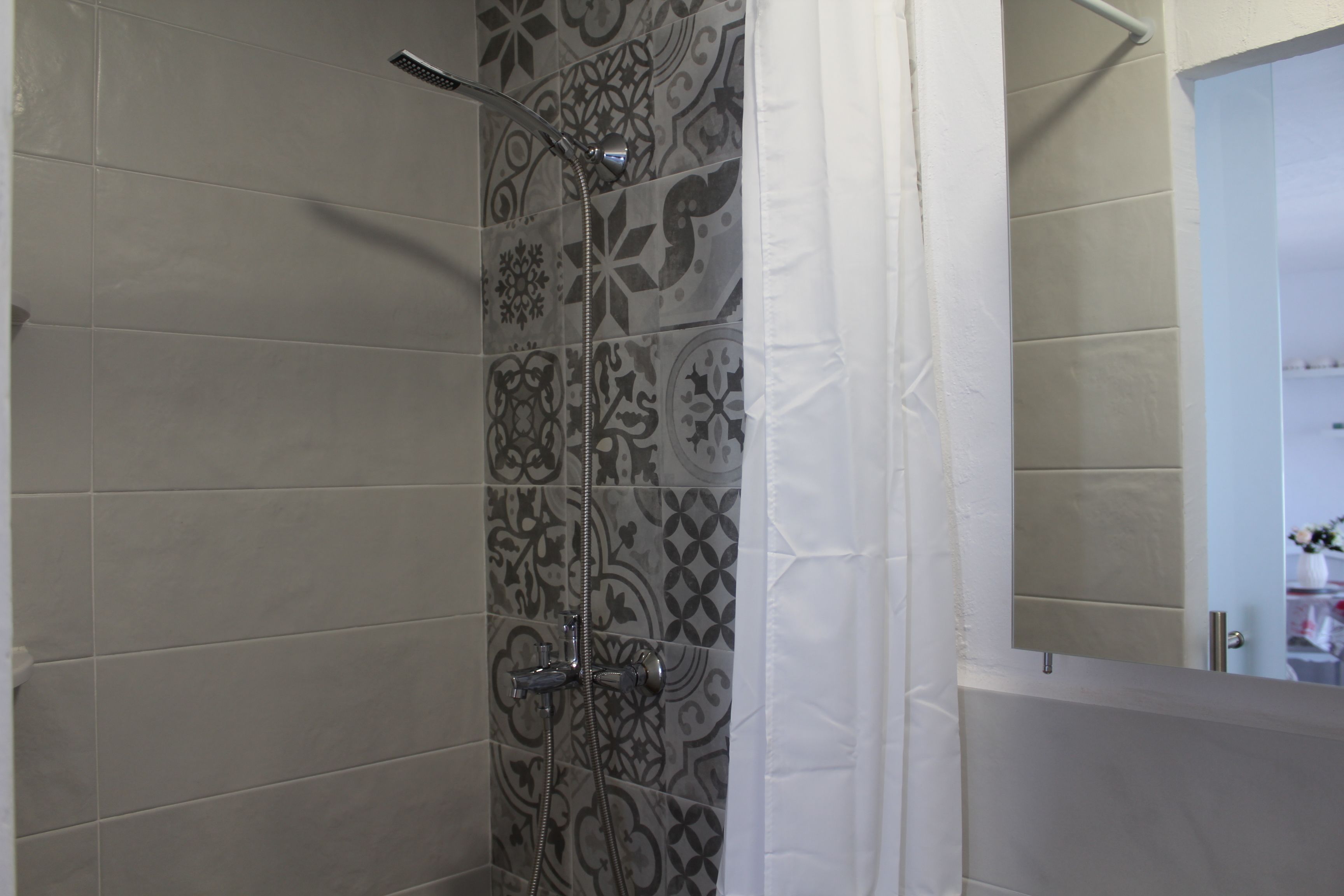 Una ducha con azulejos estampados y una cortina blanca.