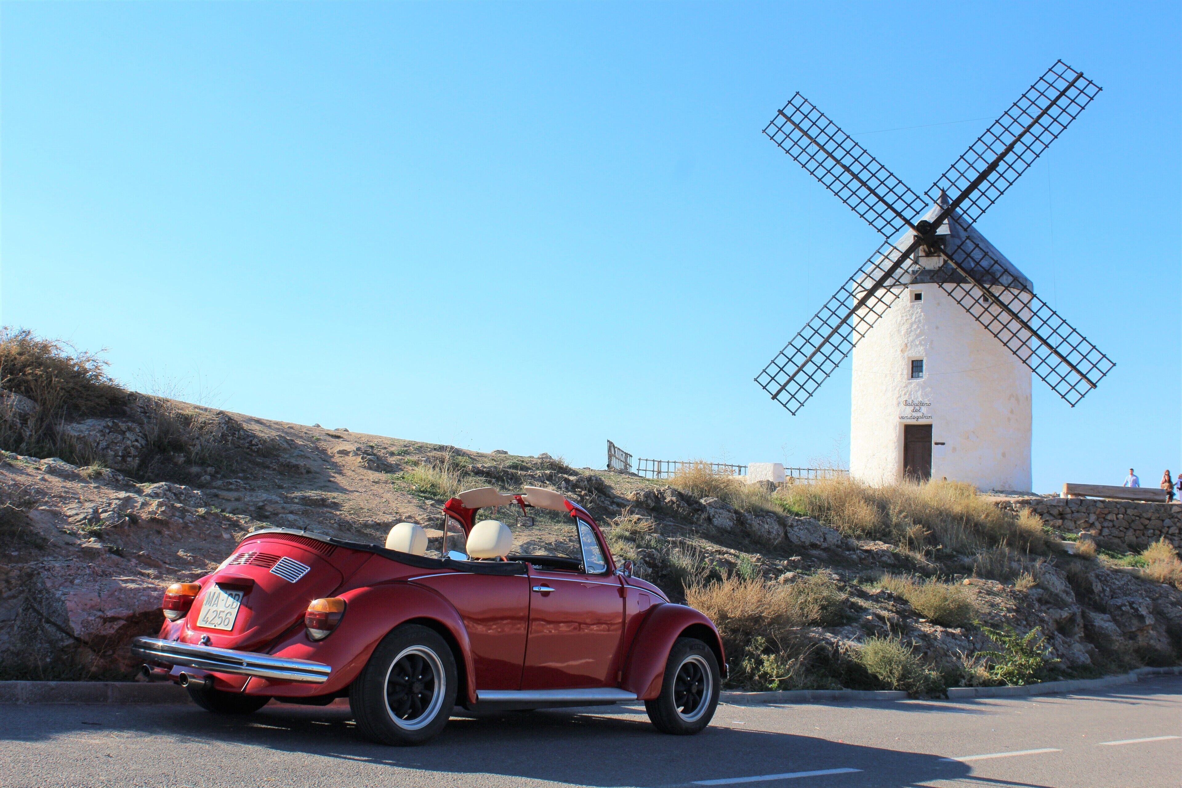 A red vintage convertible car parked on a road with a windmill in the background.