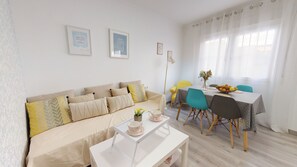 A cozy living room with a sofa, a coffee table, and a dining area with chairs and a table set for two. - Apartamentos OnceMolinos (Consuegra)