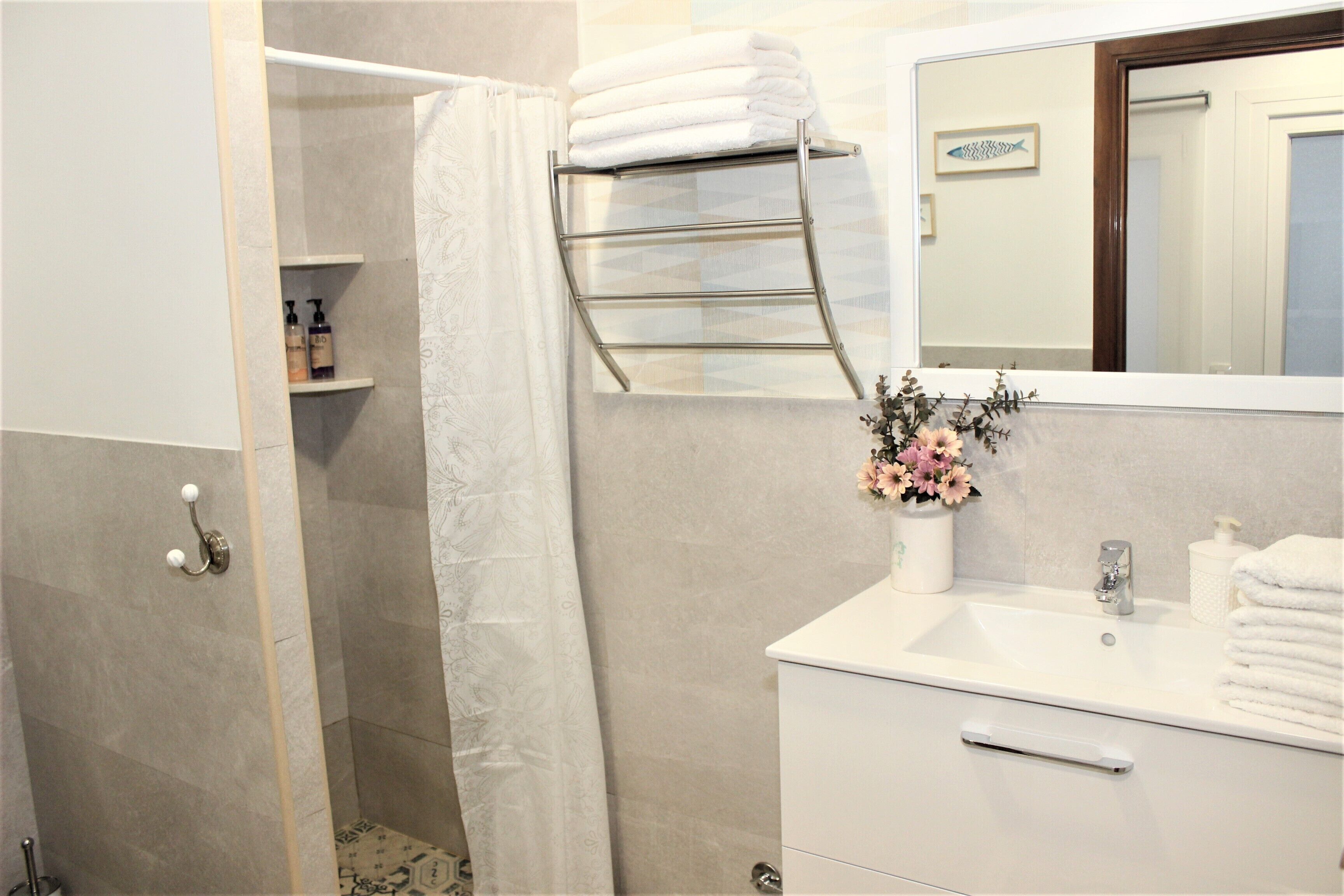 A bathroom with a shower, a towel rack, a sink, and a mirror.
