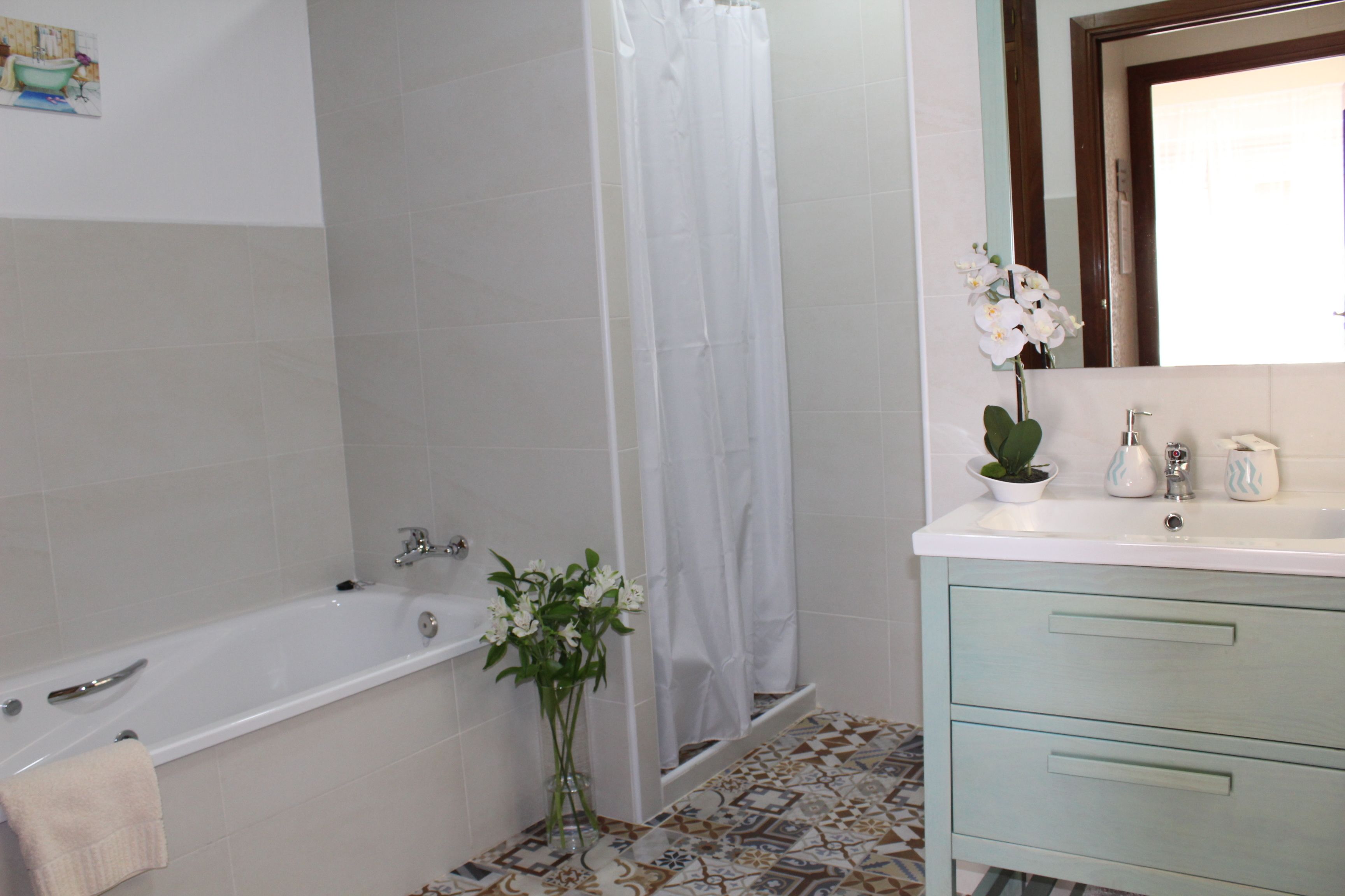A bathroom with a bathtub, a shower curtain, a sink with a mirror, and a vase with flowers.