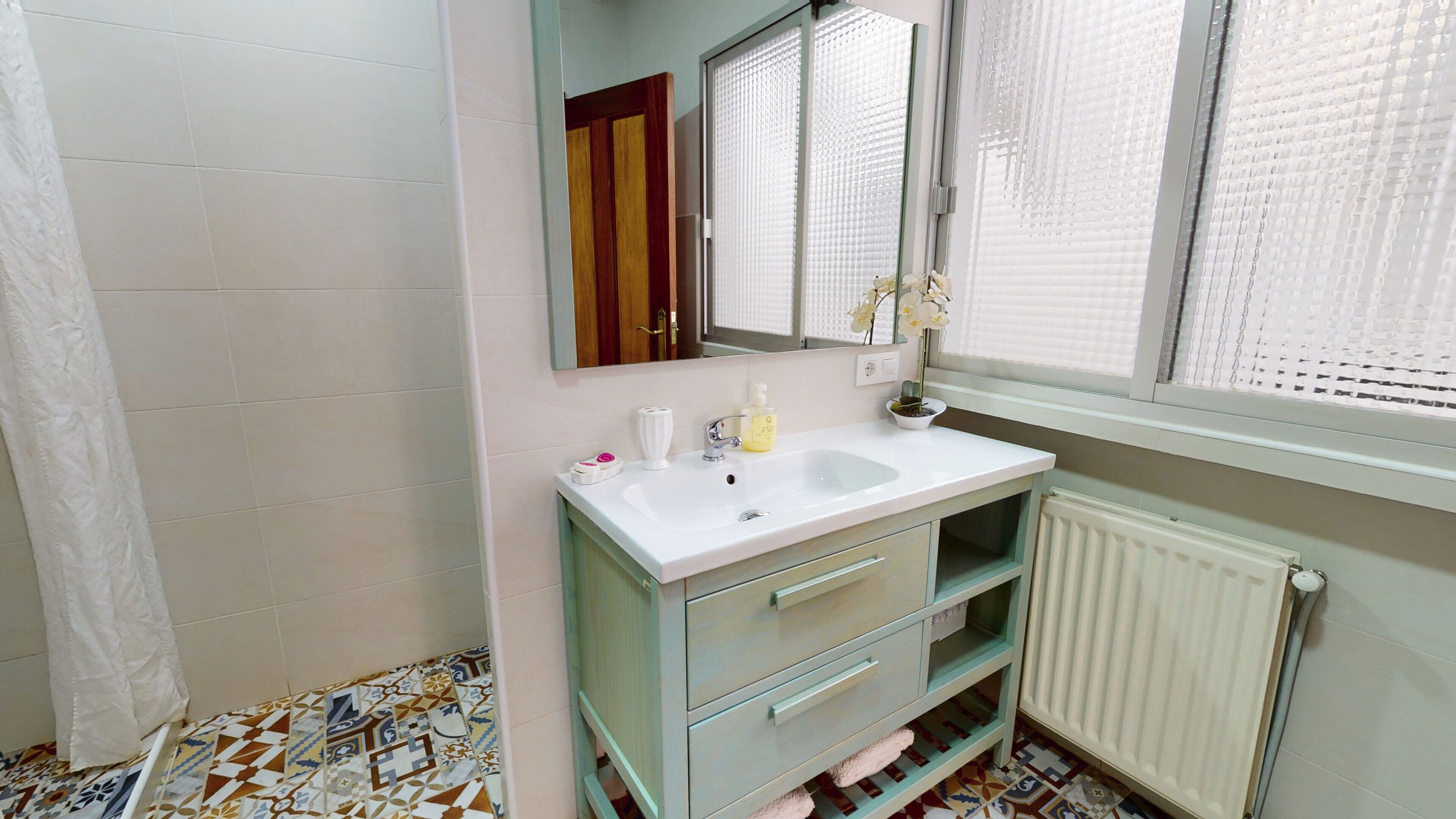 A bathroom with a white sink, a mirror, a window with blinds, and a radiator.