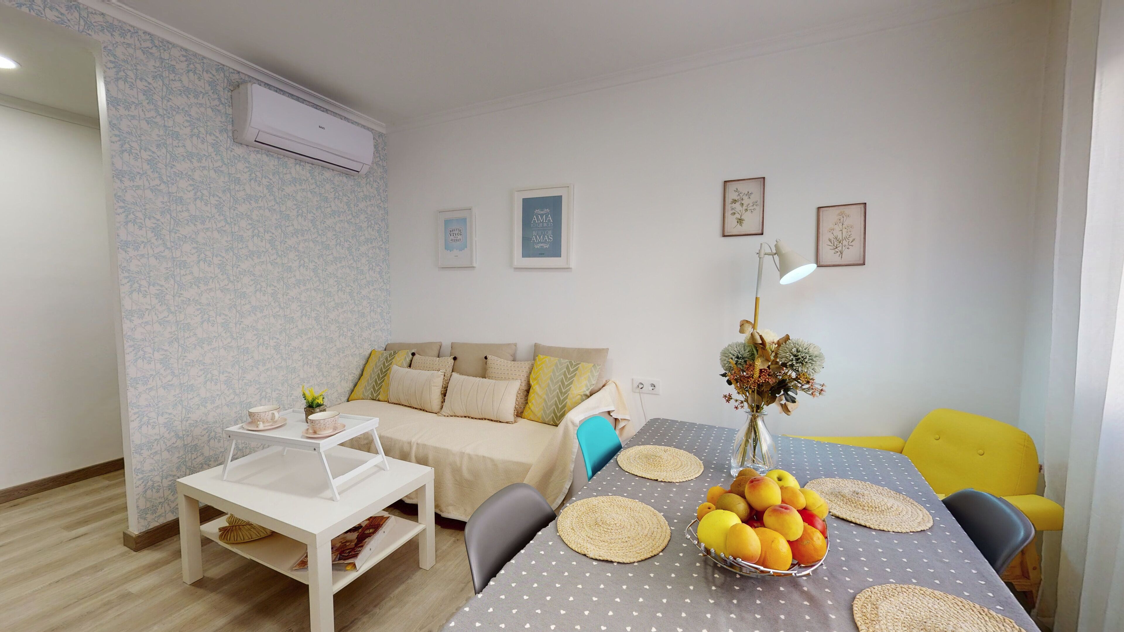 A cozy living room with a sofa, a coffee table, and a dining table set with placemats and a fruit bowl.