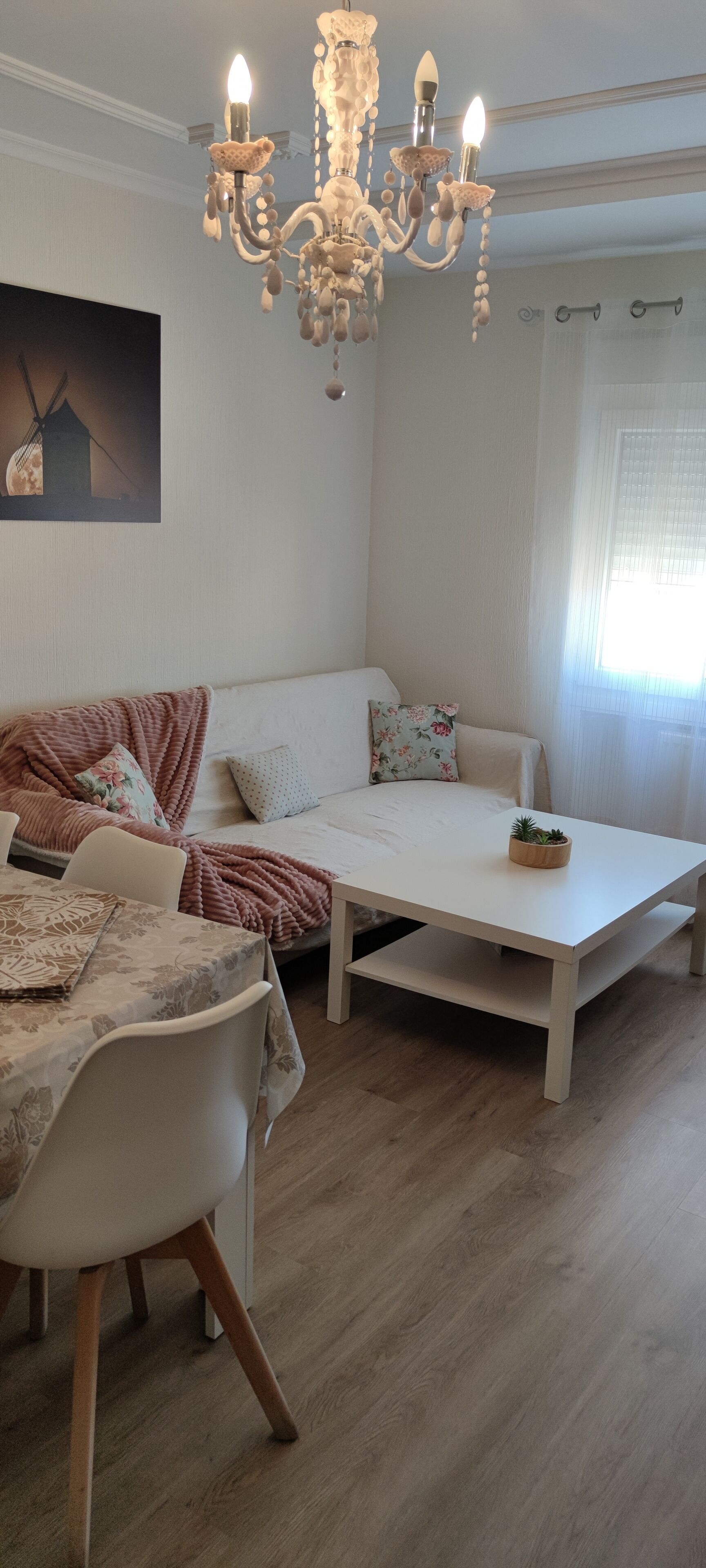 Ein gemütliches Wohnzimmer mit einem weißen Sofa, einem Esstisch und einer Deckenleuchte.