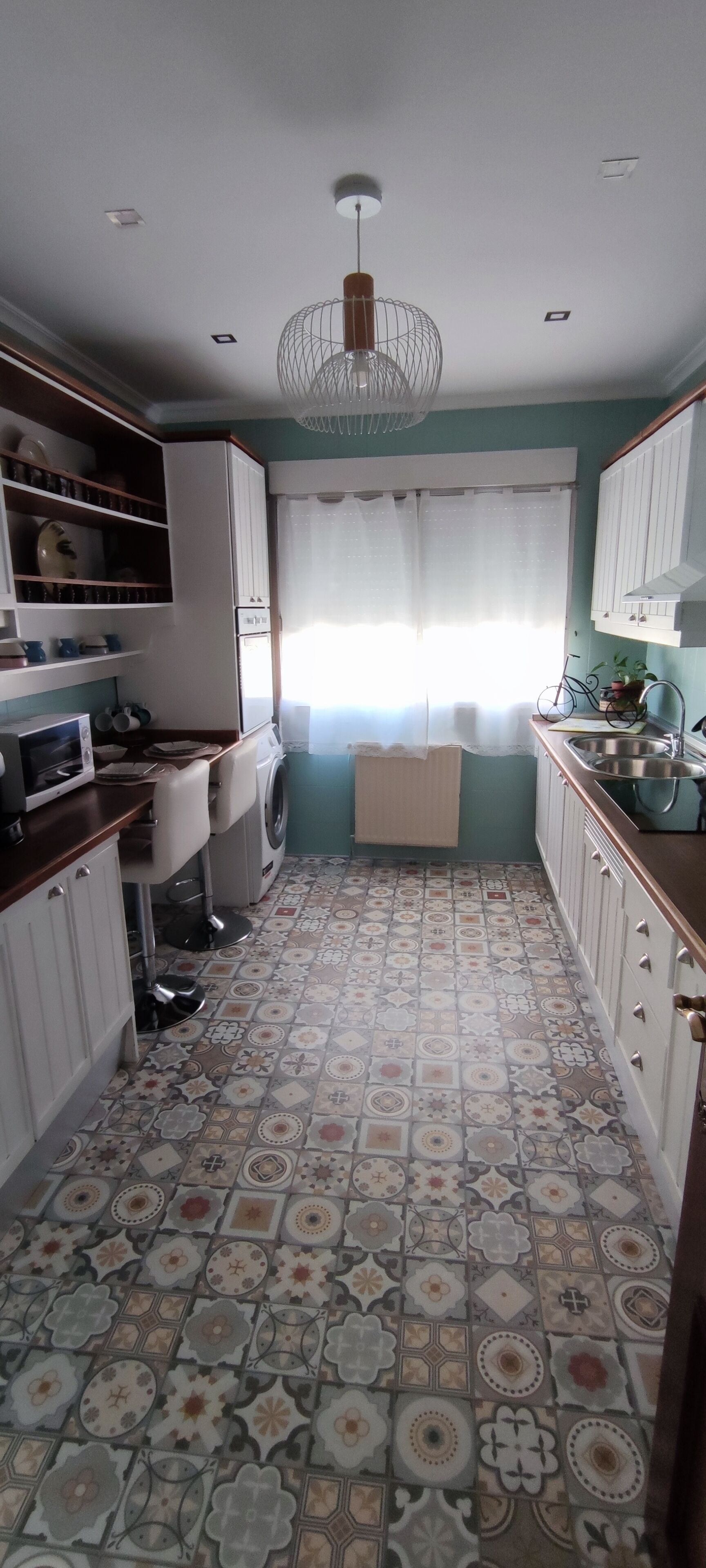 Una cocina compacta con piso de baldosas estampadas, gabinetes blancos, lavadora y ventilador de techo.