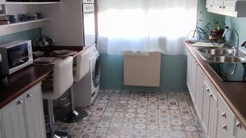 Una cocina compacta con piso de baldosas estampadas, gabinetes blancos, lavadora y ventilador de techo.