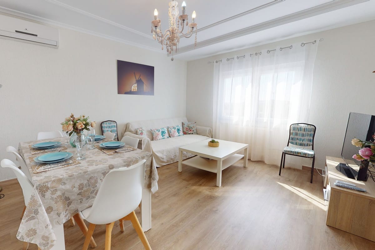 A dining area with a table set for four, a sofa, a TV, and a floor lamp.