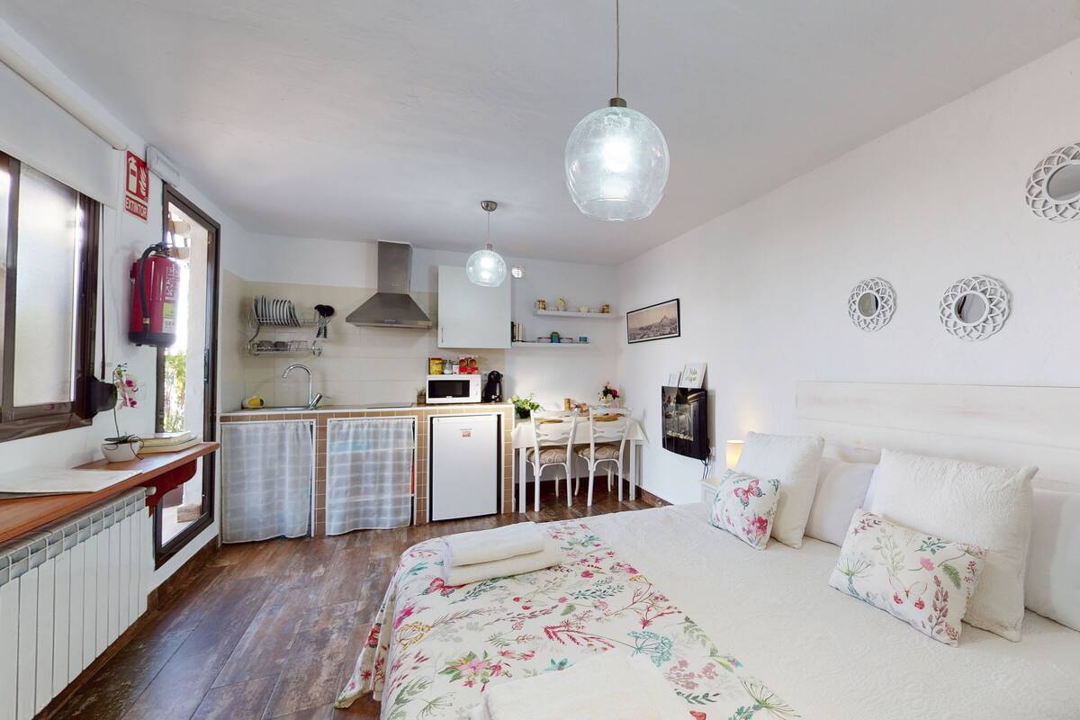 A bedroom with a bed, a bedside table, and a nightstand. There is a window with a view of the outside.