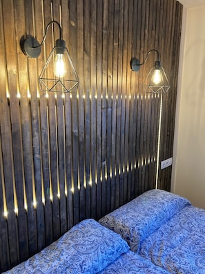 Ein Zimmer mit einer Wand aus Holzleisten, zwei Wandlampen und einer gemusterten Bettdecke.