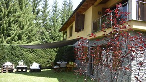 Une maison avec une façade en pierre, une terrasse en bois et un coin repas aménagé avec du mobilier d’extérieur.