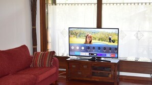 Un salon avec un canapé rouge, un meuble TV en bois et un grand téléviseur à écran plat qui diffuse une scène de paysage.