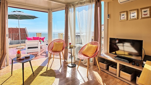 A spacious balcony with a view of the sea, furnished with a sofa, chairs, and a table.