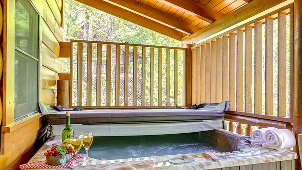 A wooden deck with a hot tub, a bench, and a table with drinks and towels. - Pool table, hot tub, 2 bedroom log cabin close to Dollywood and National Park! (Sevierville)