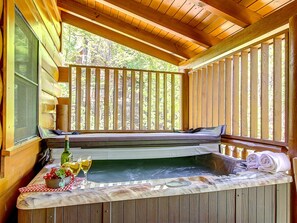 A wooden deck with a hot tub, a bench, and a table with drinks and towels.