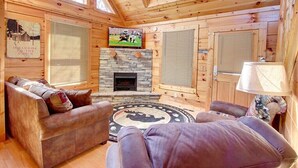 A log cabin interior with a fireplace, wooden walls, and a television mounted above it. - Pool table, hot tub, 2 bedroom log cabin close to Dollywood and National Park! (Sevierville)