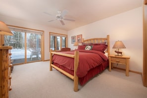 A bedroom with a wooden bed, two bedside tables, a ceiling fan, and a large window with a view of trees.