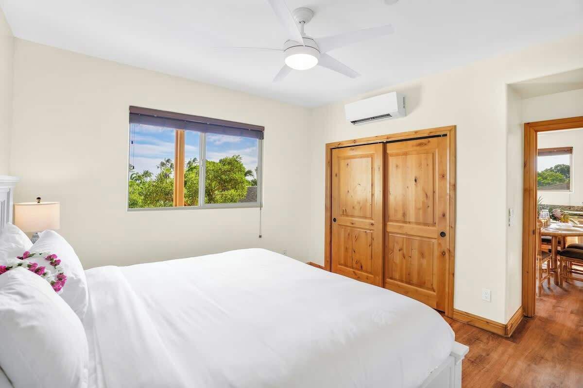 A bedroom with a bed, a window with a view, a ceiling fan, and a wooden door.