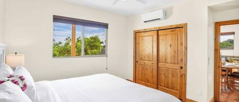 A bedroom with a bed, a window with a view, a ceiling fan, and a wooden door.
