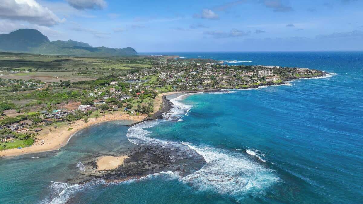 Luchtbeeld van een kustplaatsje met een strand, oceaan en een bergachtig achtergrond.