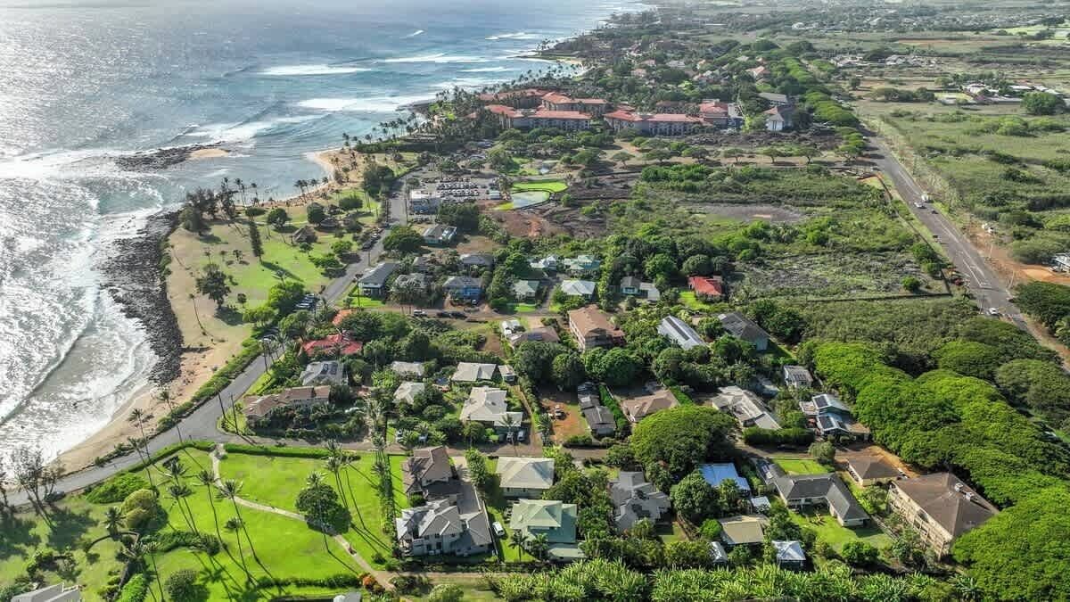 An aerial view of a coastal residential area with houses, a beach, and a road.