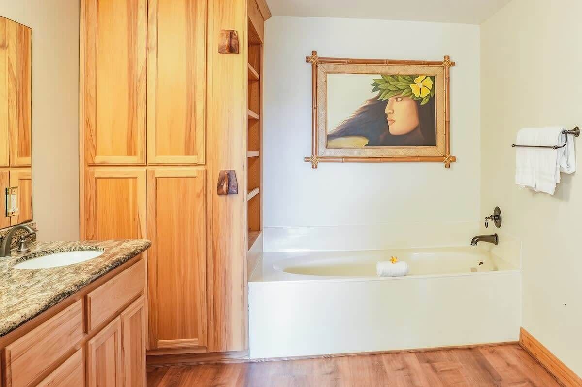 A bathroom with wooden cabinets, a sink, a bathtub, and a framed picture on the wall.