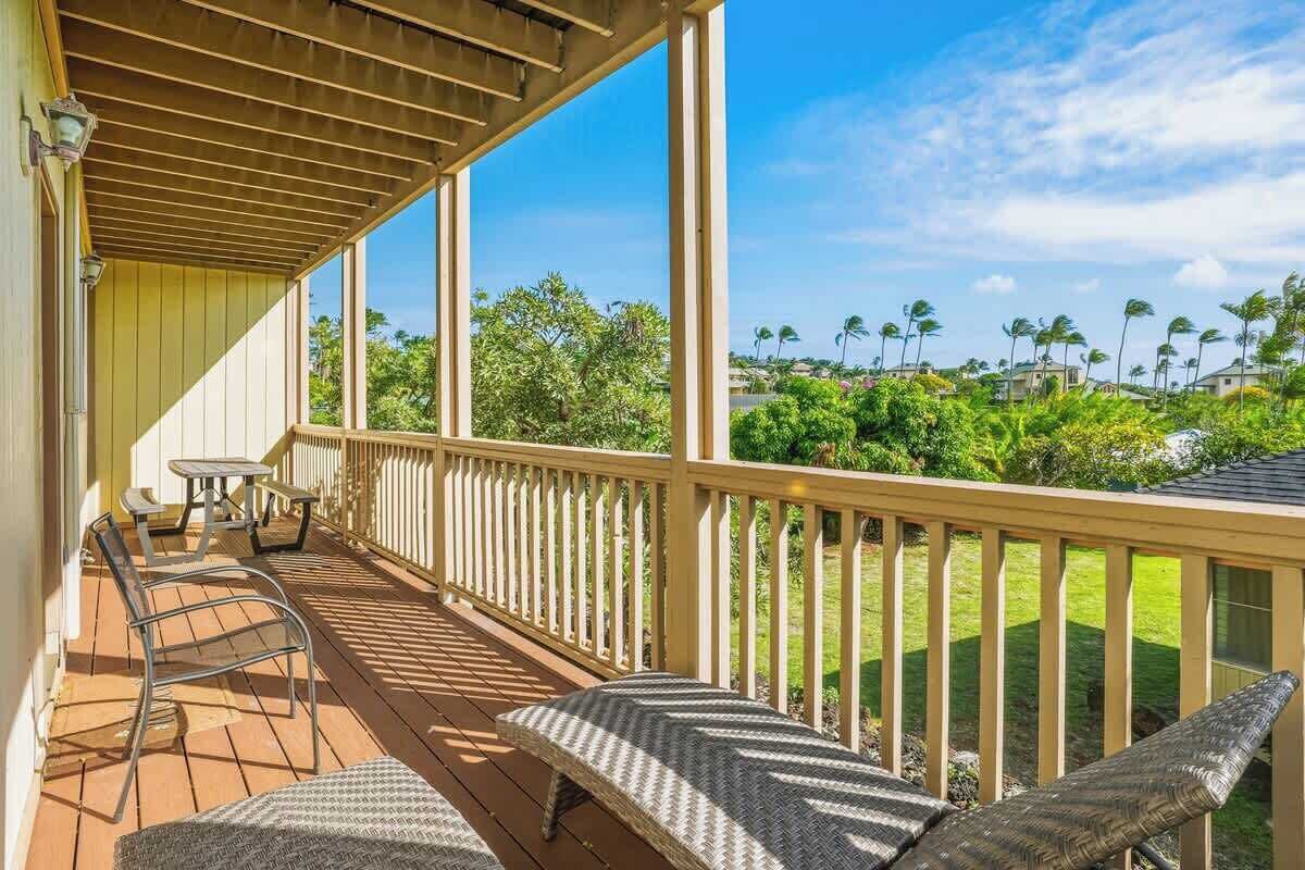 A covered outdoor deck with a table and chairs, a bench, and a view of a green landscape with trees and houses.