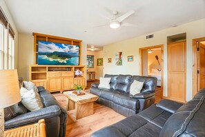 A living room with a large flat-screen TV, leather sofas, wooden coffee table, and a ceiling fan.