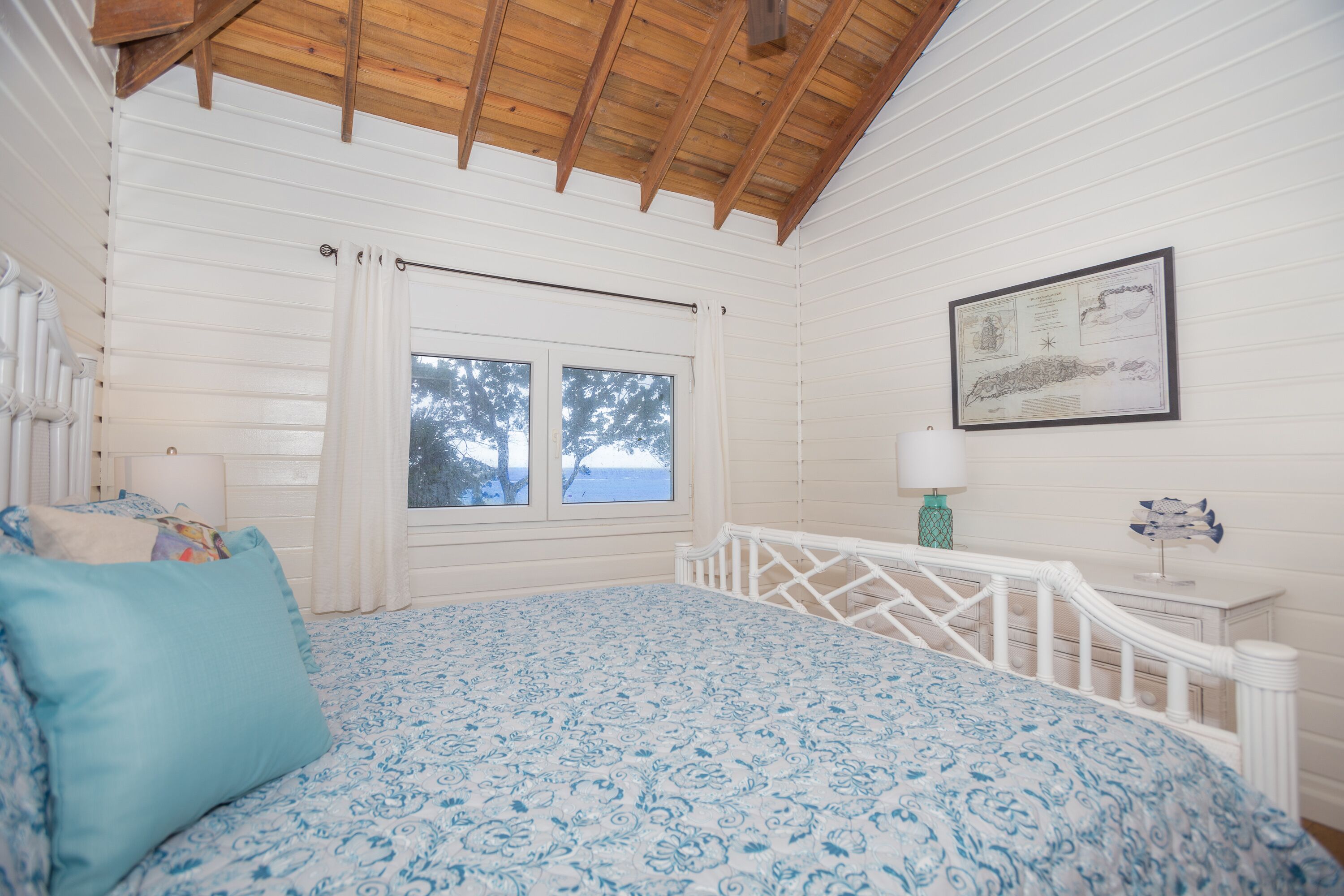 A bedroom with a bed, a window, a white railing, and a framed picture on the wall.