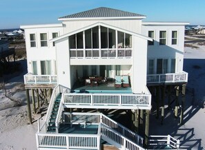 A two-story beach house with a balcony and a deck, featuring a staircase and outdoor seating. - Sailfish | Last minute opening 8/4. Gulf Front (Dauphin Island)