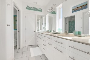 A modern bathroom with a large mirror, a vanity with multiple drawers, and a shower area. - Sailfish | Last minute opening 8/4. Gulf Front (Dauphin Island)