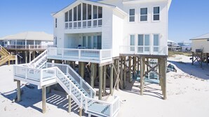 Een twee verdiepingen tellend strandhuis met een balkon en een trap die naar de bovenverdieping leidt.