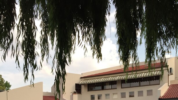 Un espace piscine comprenant des chaises longues, une table et un bâtiment doté d’un toit et de fenêtres recouverts de tuiles.