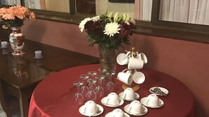 Une table ronde recouverte d’une nappe rouge, un vase rempli de fleurs, ainsi que des tasses et des soucoupes à thé blanches disposées dessus.