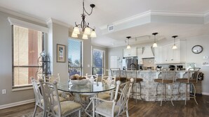 Een ruime keuken met een centraal eiland, witte kasten en een eethoek met een glazen tafel en witte stoelen.