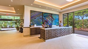 Un comptoir d’accueil moderne, avec deux employés, de grandes fenêtres et une vue sur la verdure à l’extérieur.