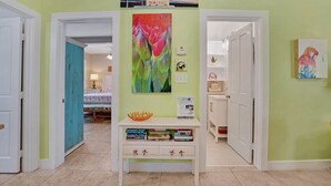 A hallway with a white console table displaying books and a colorful painting. - **THE MELLOW MACAW** Cozy Condo Near Duval + Last Key White Glove Service... (Key West)