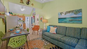 A cozy living room with a striped sofa, a dining area with a table set for two, and a kitchen with modern appliances. - **THE MELLOW MACAW** Cozy Condo Near Duval + Last Key White Glove Service... (Key West)