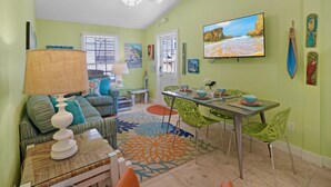 A bright living room with a sofa, dining table, and chairs. There is a TV on the wall and artwork on the walls. - **THE MELLOW MACAW** Cozy Condo Near Duval + Last Key White Glove Service... (Key West)