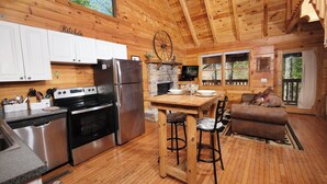 A wooden cabin interior with a kitchen, dining area, and living space. - POOL TABLE, HOT TUB, AND JACUZZI TUB in a CONVENIENT location! (Sevierville)