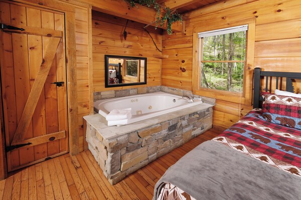 Relax in this serene cabin bedroom with a bathtub, large door, and forest view.