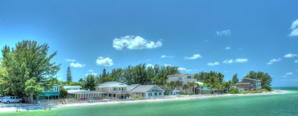 Un hotel frente al mar con varias construcciones, una playa y cielos despejados.