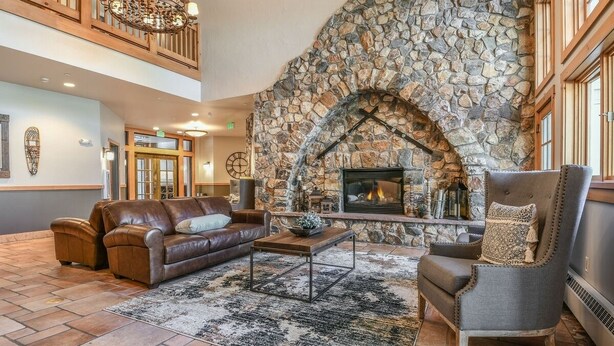 A spacious living area with a stone fireplace, leather sofas, and a chandelier. - Bright Corner Unit in River Run/Walk to the Slopes/Pool and Hot Tub Access (Keystone)