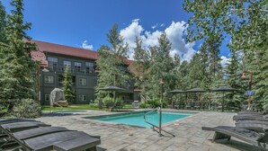 A pool area with lounge chairs and a building in the background. - Bright Corner Unit in River Run/Walk to the Slopes/Pool and Hot Tub Access (Keystone)