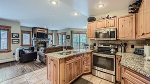 A spacious kitchen with wooden cabinets, granite countertops, stainless steel appliances, and a cozy seating area with a fireplace. - Bright Corner Unit in River Run/Walk to the Slopes/Pool and Hot Tub Access (Keystone)